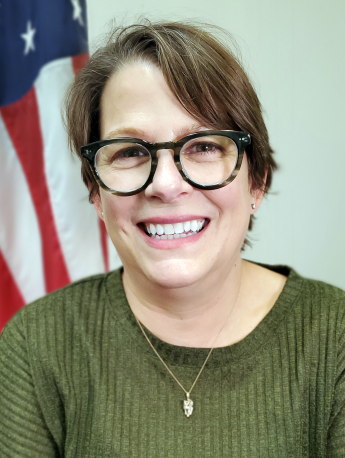 Person with glasses, smiling big, in front of an American flag.