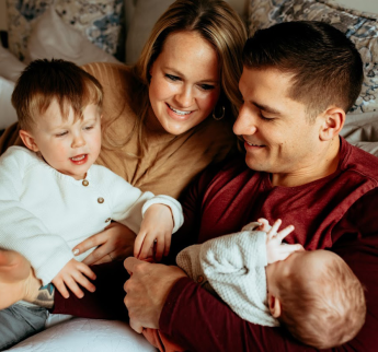 Kylie Ferraz with her husband, Brandon, hold their two small children on a couch.