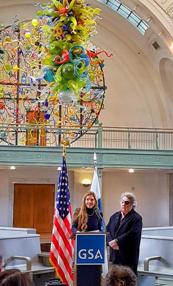 Two people at a GSA podium, standing under an intricate, colorful glass art fixture