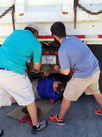 Men inspect a vehicle and install a front license plate