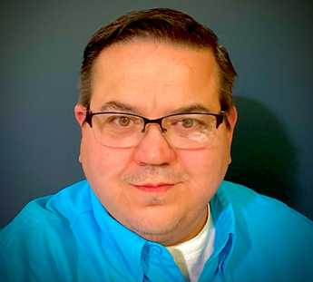 Tight headshot of a person wearing glasses and a blue, collared business shirt.