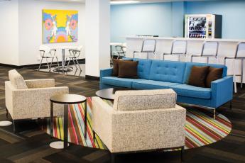 Photo showing an office sitting area with a couch and chairs in the foreground, with tables and a bar counter in the background.