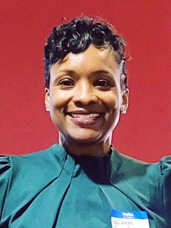 Smiling Black woman with short hair and wearing a teal top in front of a red background