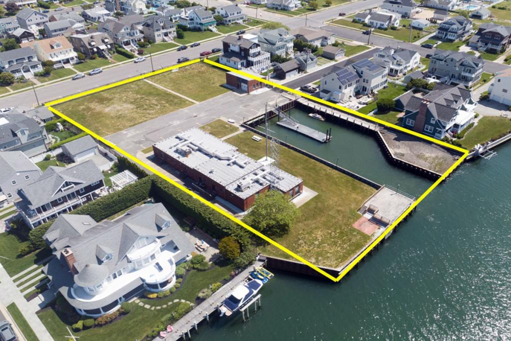 Aerial view of a red brick office building surrounded by a seawall and boat basin with a small dock on river. A square yellow border.