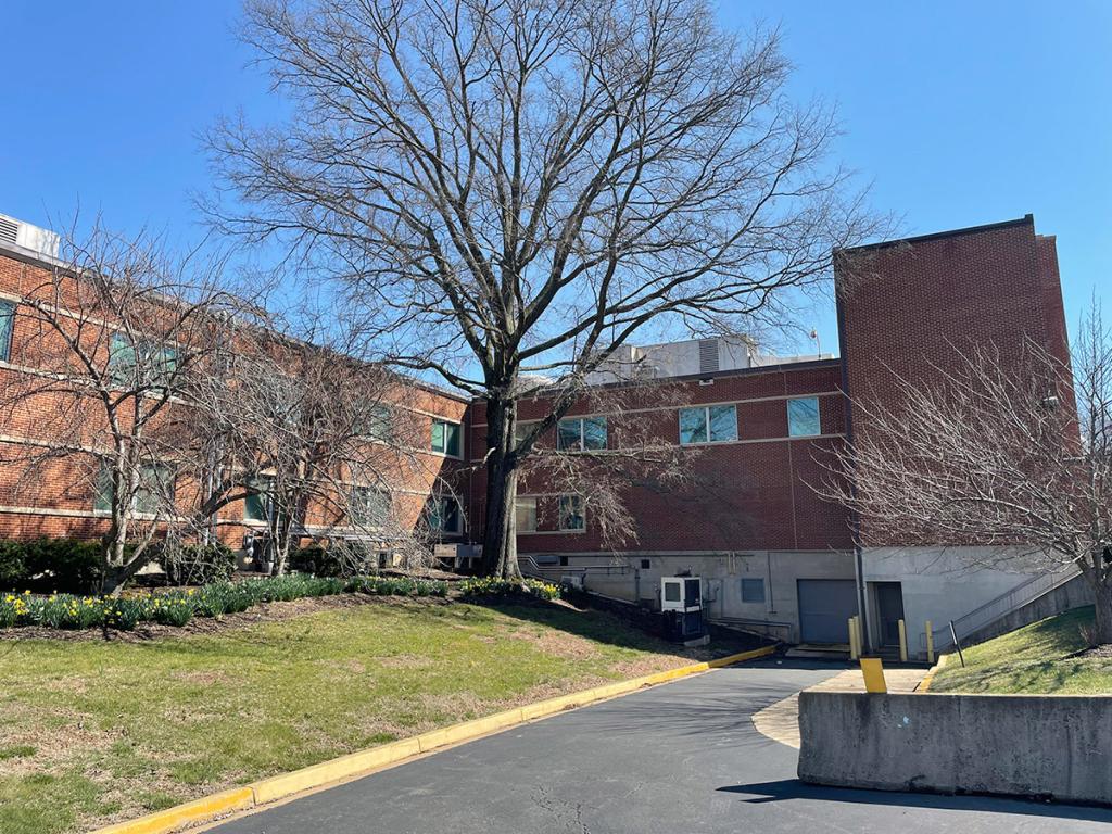 Two-level red brick building with a tree, grass, flowers and pavement in front
