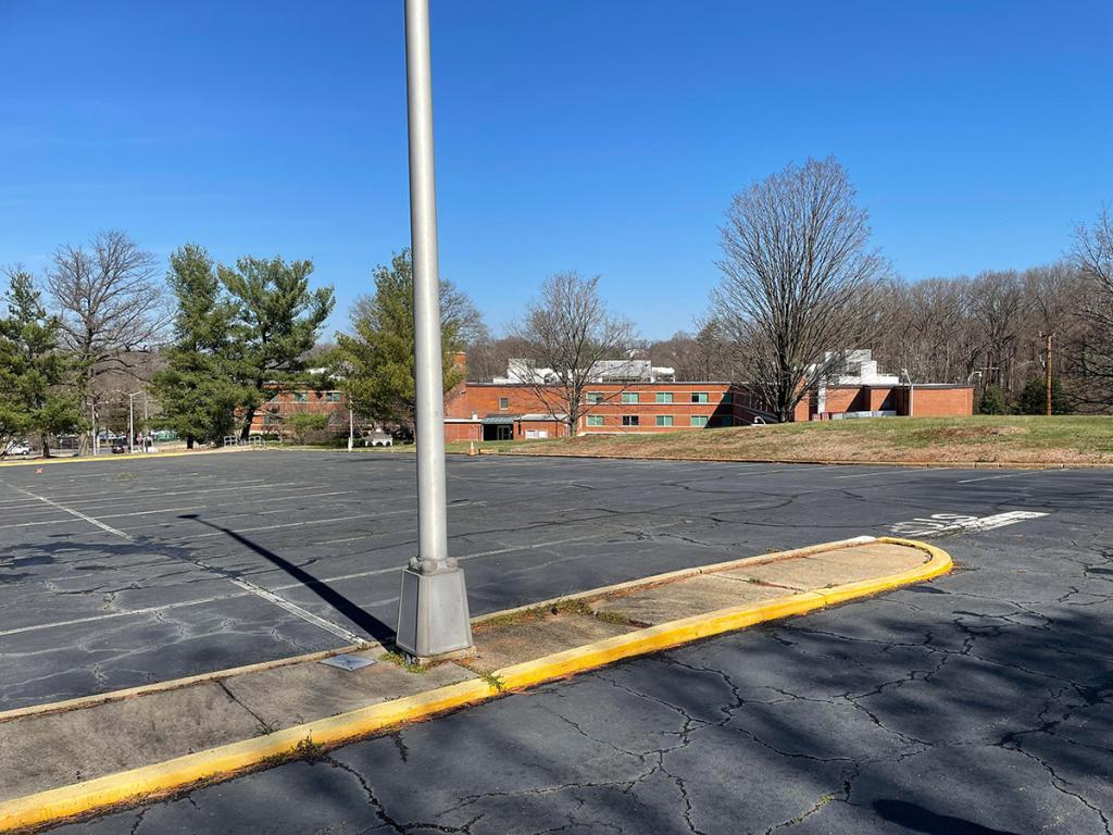 Parking lot with lamp post in foreground, with low red brick building in background, with trees and grass