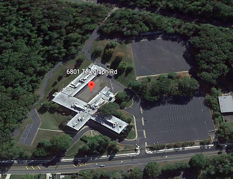 Aerial view of an F-shaped building and parking lots with a road, trees and grassy areas around it, and a map marker indicating 6801 Telegraph Rd