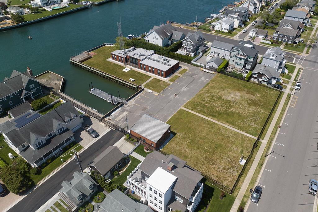 One-story brick building on a river with seawall, deck, boat basin, dock, fence, parking lot, maintenance building. Large lawn near street.