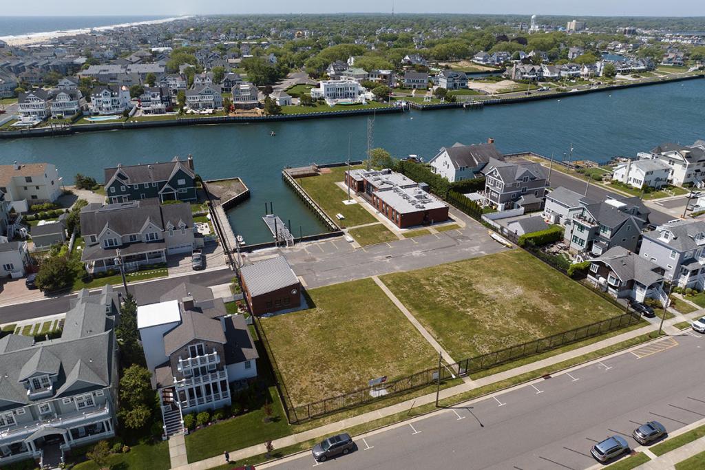 One-story brick building on river with seawall, deck, boat basin, dock, fence, parking lot, maintenance building. River stretches inland.