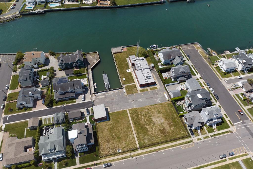 One-story brick building on river with seawall, deck, boat basin, dock, fence, parking lot, maintenance building. Houses on river.