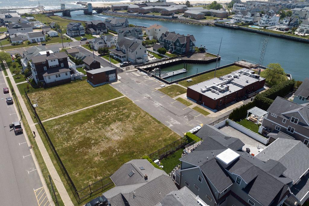 One-story brick building with seawall, deck, boat basin, dock, fence, parking lot, maintenance building. A river leads to a bridge.