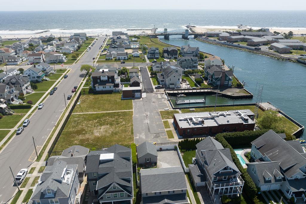 One-story brick building with seawall, deck, boat basin, dock, fence, parking lot, maintenance building. A river leads to a beach and ocean.