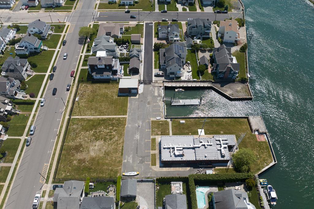 One-story brick building with seawall, deck, boat basin, dock, fence, parking lot, maintenance building. Cars parked on street near houses.