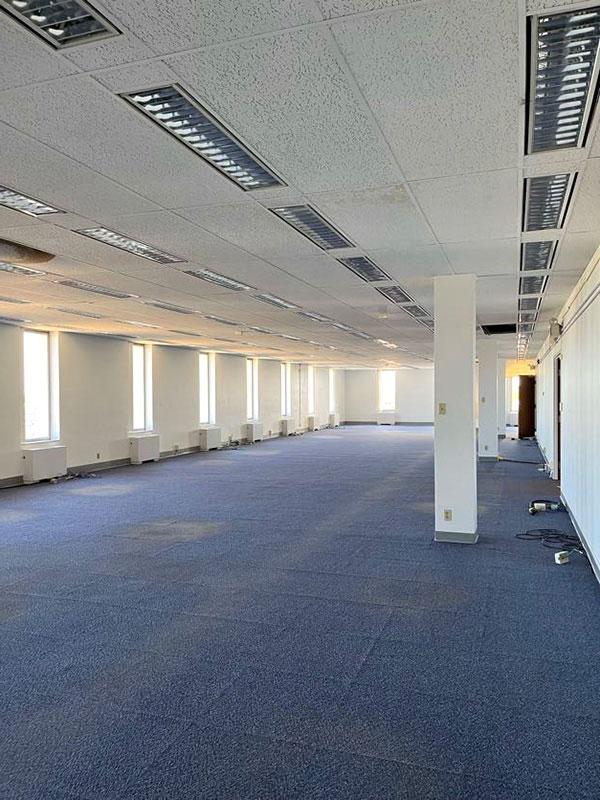 View of an interior open space with blue carpet, windows, and no funiture.