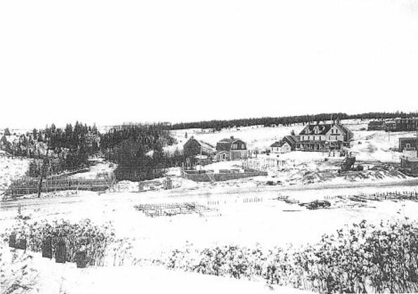black and white photo with small houses in the background with an open field in front