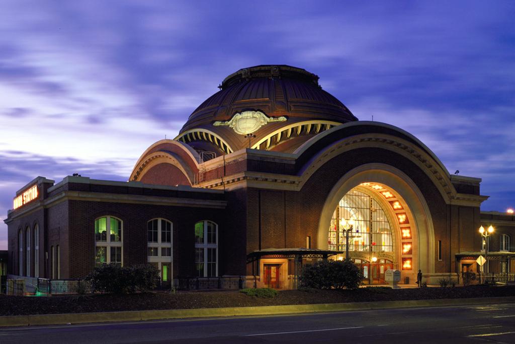 Red brick, ornate, domed building with glass, arched entrance and a sign Union Station on the left side, at dusk, lights on, in front of a vivid purple sky