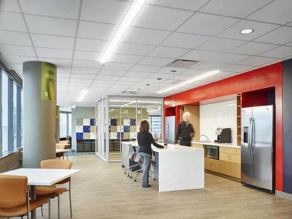 A large, open kitchen area with two people on either side of a bar with stools, and kitchen appliances along a counter and wall containing t