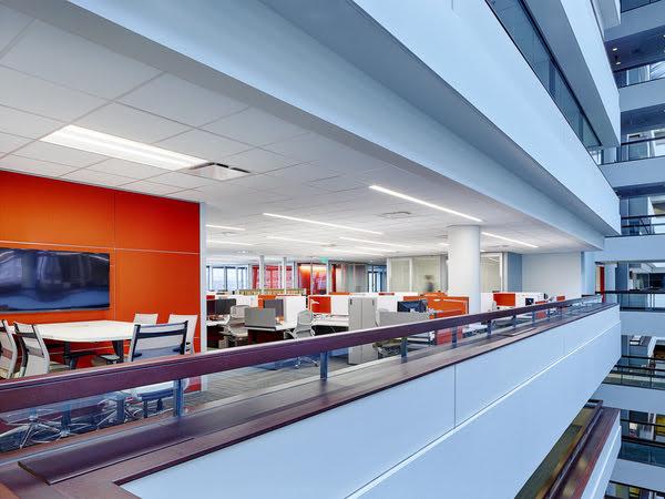 The interior of a multi-level office space, with a side view of one floor with several cubicles, a conference table and chairs with a bright