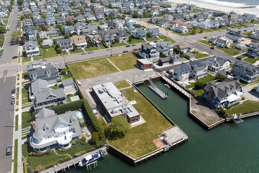 Aerial view of red brick office building surrounded by a seawall and boat basin with a small dock on a river and parking lot.