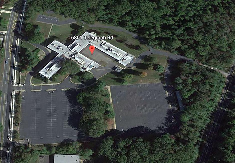 Aerial view of an F-shaped building and parking lots with roads, trees and grassy areas around it, and a map marker indicating 6801 Telegraph Rd