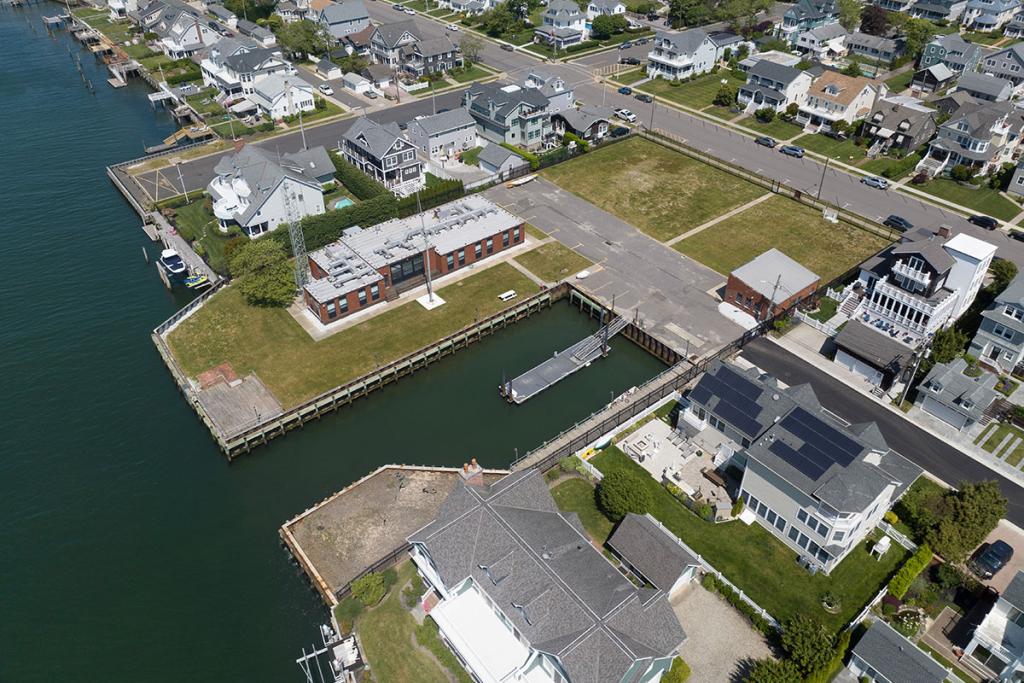 One-story brick building on river with seawall, deck, boat basin, dock, parking lot and maintenance building. Two houses on basin.