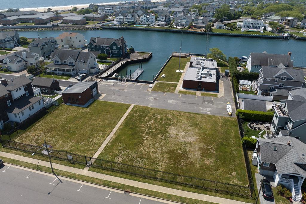 One-story brick building on river with seawall, deck, boat basin, dock, fence, parking lot, maintenance building. Large lawn near fence.