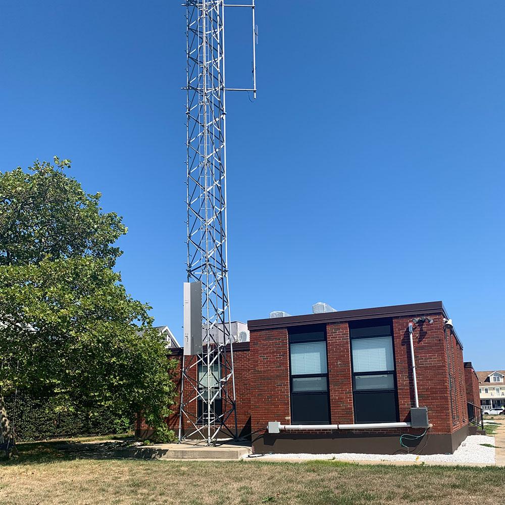 A large communications tower stands near a single-story red-brick building with multiple windows.