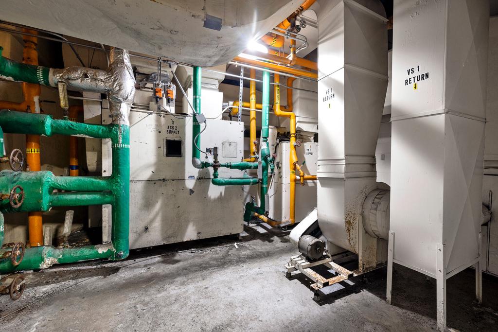 Multiple vents and green and yellow pipes in a concrete boiler room.