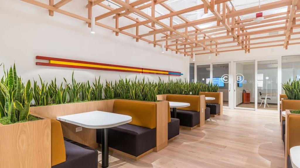 Booths lined with plants and a wood patterned floor with wood framing at the ceiling and office spaces and conference rooms.