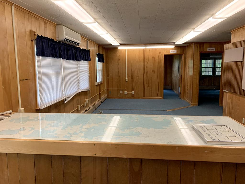 Empty room interior with natural wood paneling, acoustic tile ceiling, and blue carpeting, with a desktop showing a map