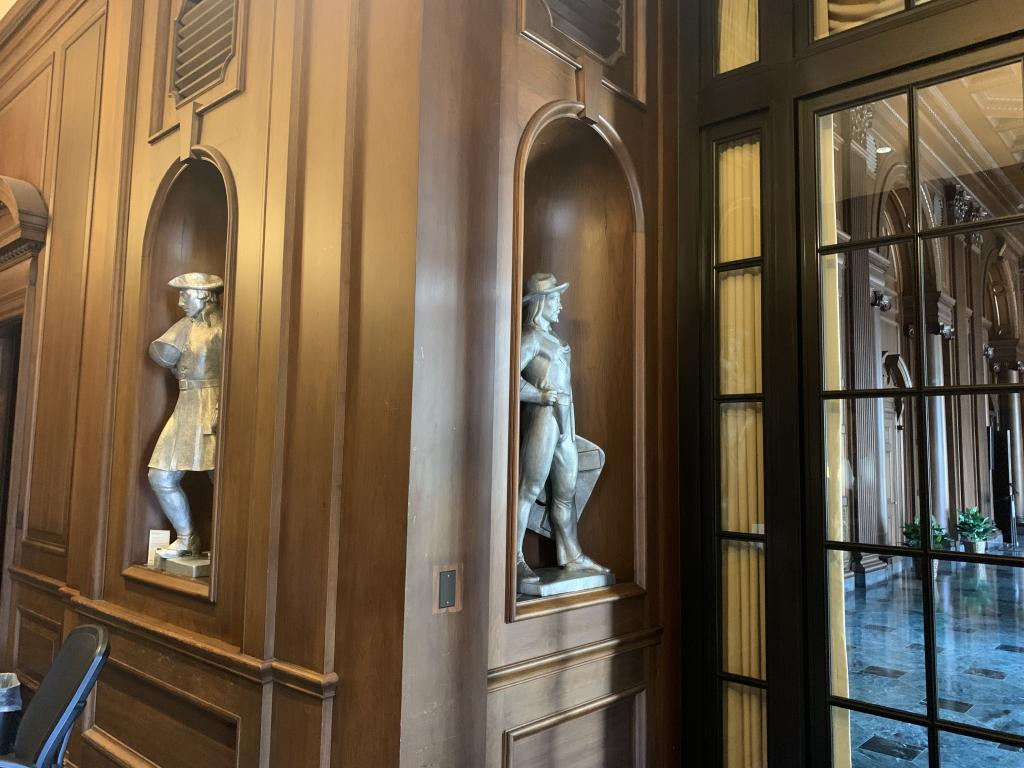 two aluminum sculptures set into niches located in a grand room with wood paneling