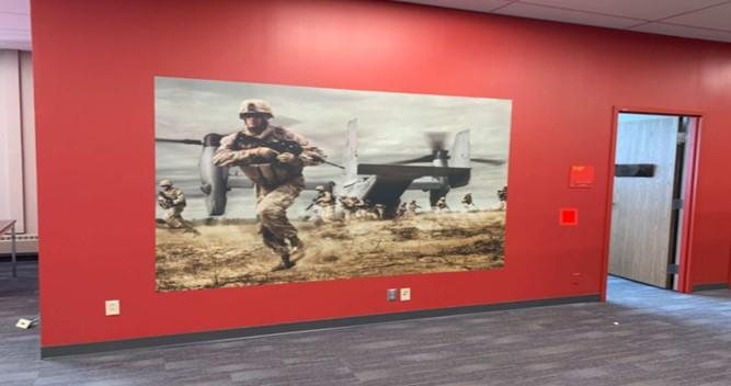Marine Corps Enterprise Information Technology Services administrative space with a painted mural featuring Marines in a field with a CV-22 Osprey aircraft.