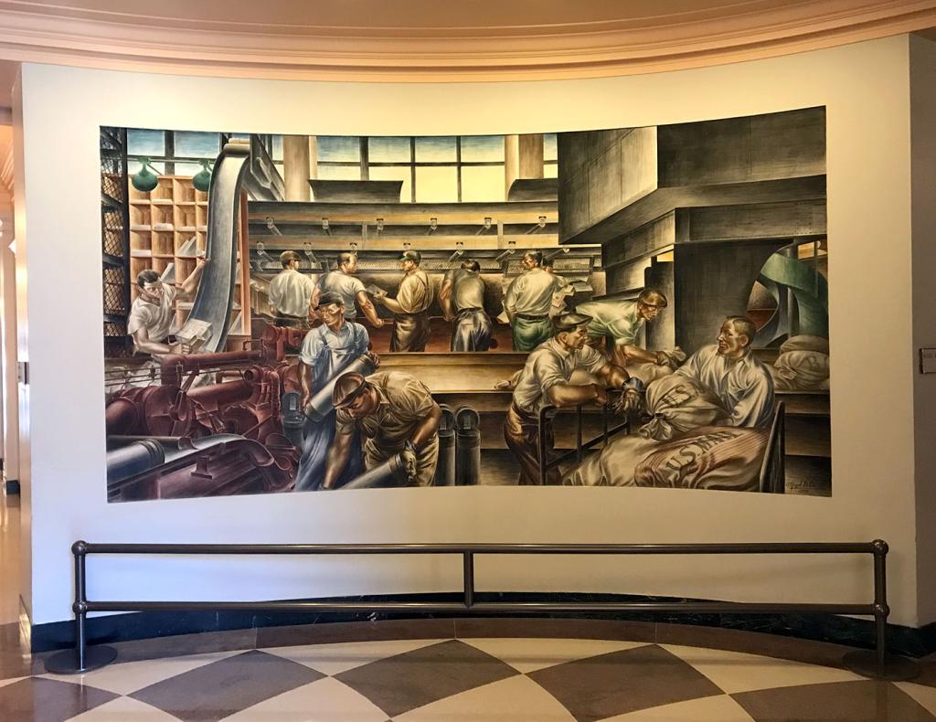 Large fresco mural by Alfredo Di Giorgio Crimi, showing eleven men working in a post office facility, sorting and moving bags of mail, 1937