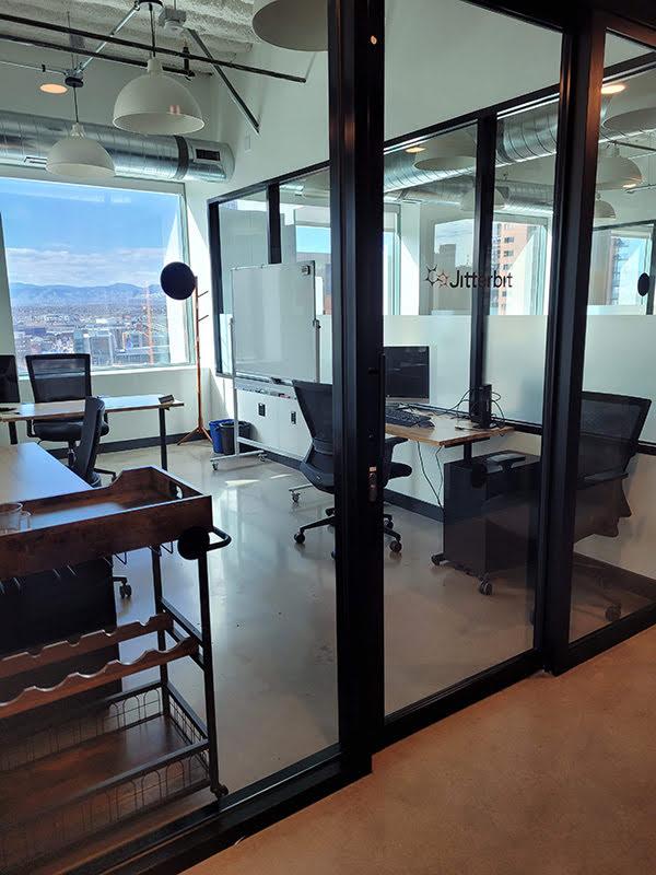 A glass-walled office space with the word Jitterbit on the glass door; the office has a wooden serving rack along the near wall 