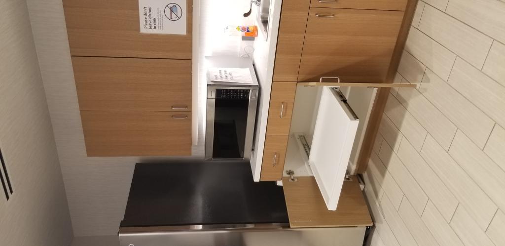 An empty lower cabinet slide out drawer under a microwave in a break area.