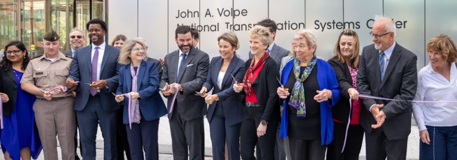 many people line up to cut the ribbon and a ceremonial event in front of the new Volpe Transportation Center in Cambridge MA